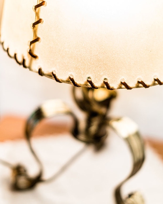 Close-up of a lit lamp with a beige stitched lampshade and ornate metal base.