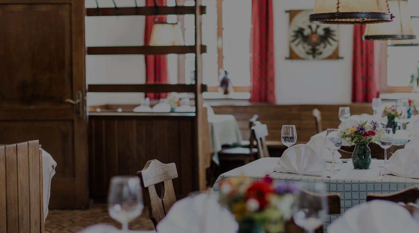 An elegant restaurant dining room featuring tables set with white linens, wine glasses, and fresh flower bouquets.