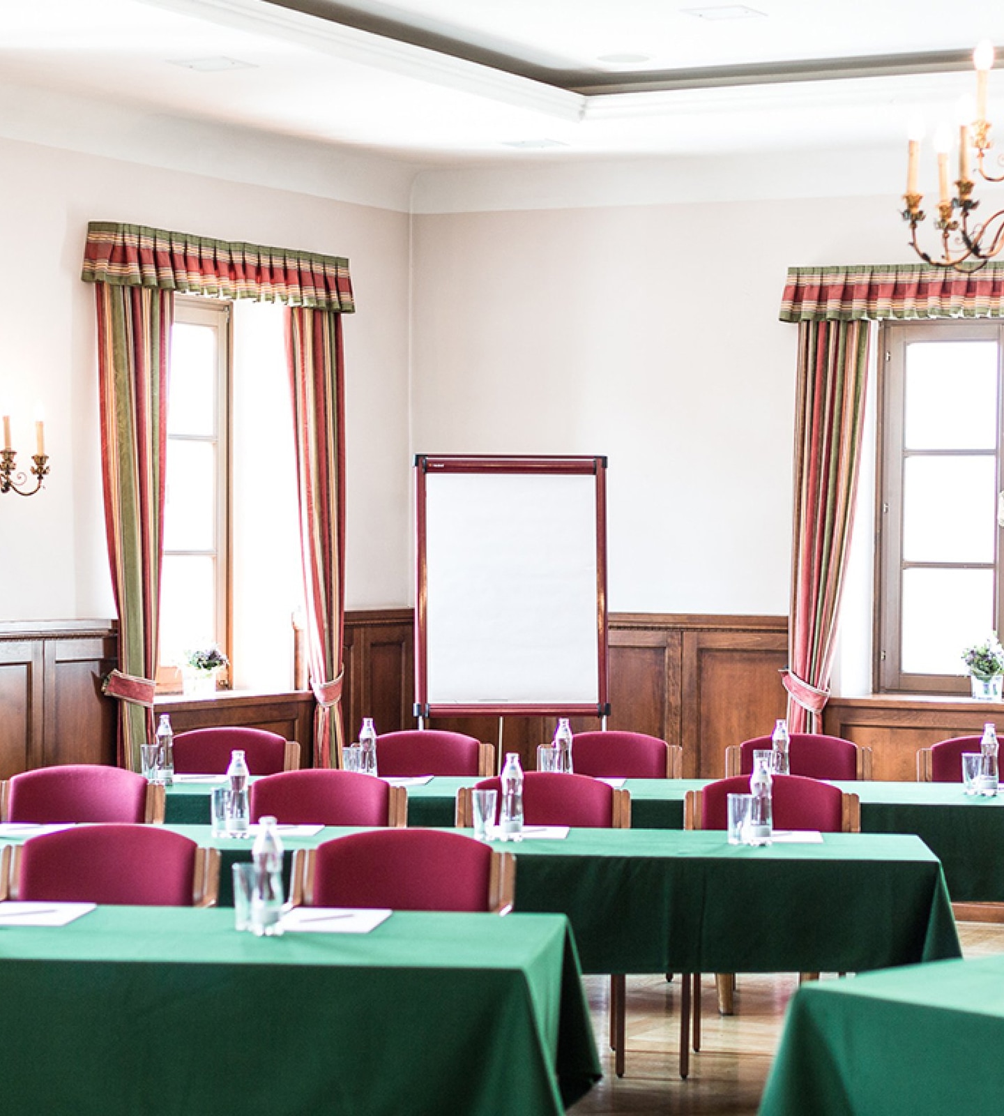 An elegant meeting room set up with green tablecloths, red chairs, and a blank whiteboard.