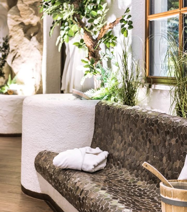 Tiled heated bench with white robe in a spa relaxation room next to plants.