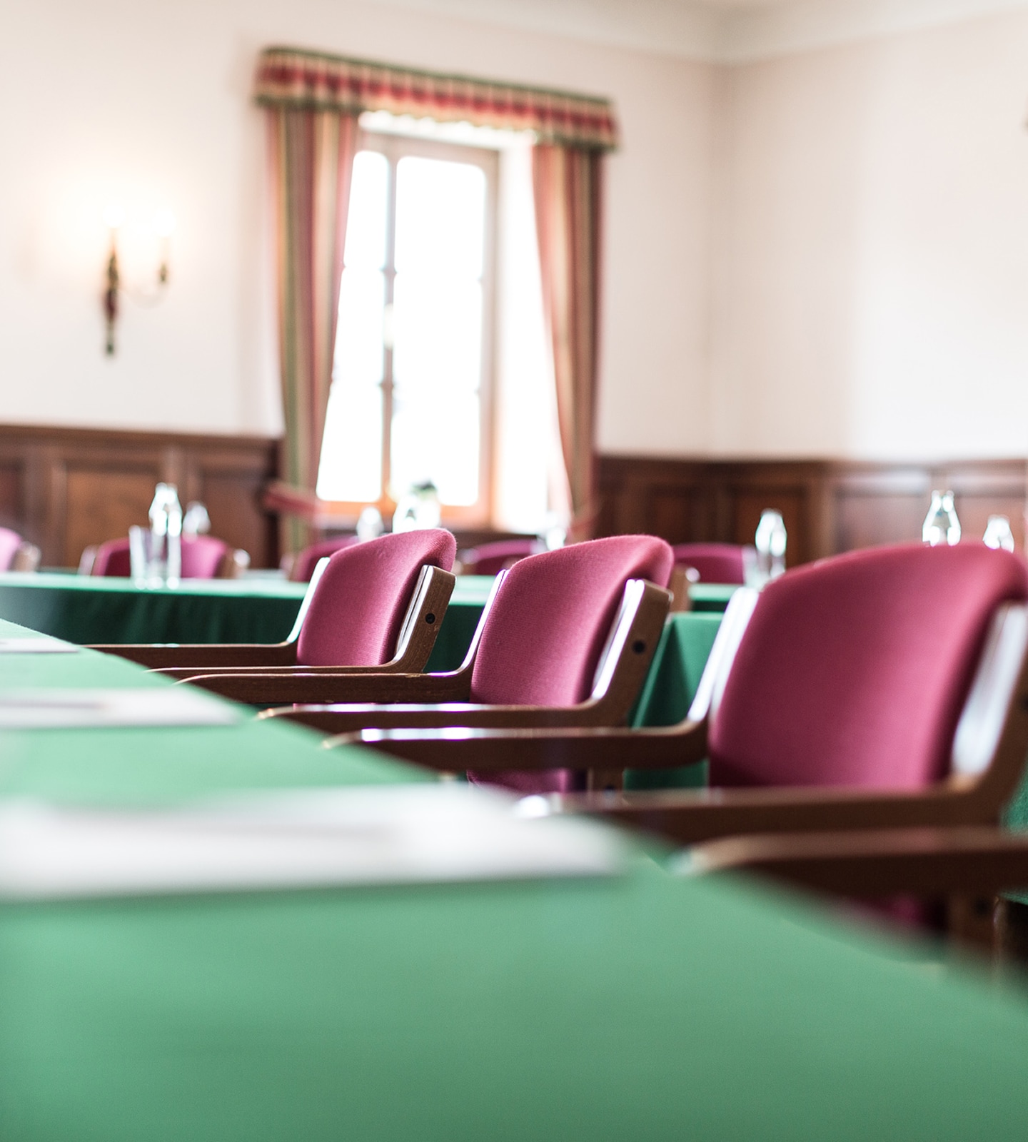 Close-up of pink upholstered conference chairs with wooden arms at tables with green tablecloths.