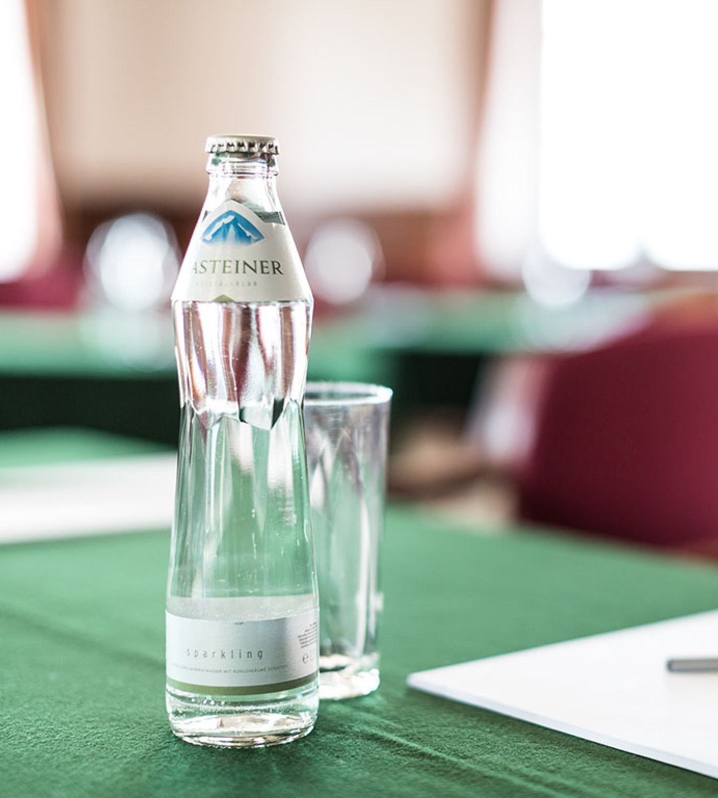 A bottle of Gasteiner sparkling water next to an empty glass on a green tablecloth.