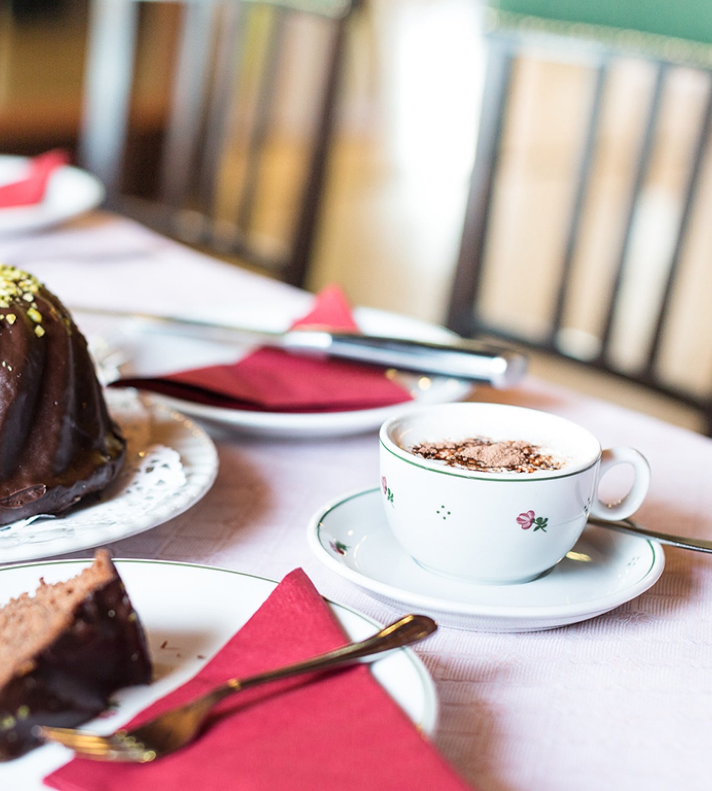 A white floral coffee cup on a saucer next to chocolate bundt cake and a slice of cake on a plate.
