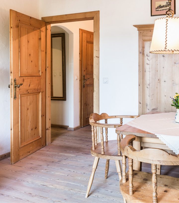 Cozy rustic dining area with wooden table, chairs, and paneling next to open doorways showing a hallway.