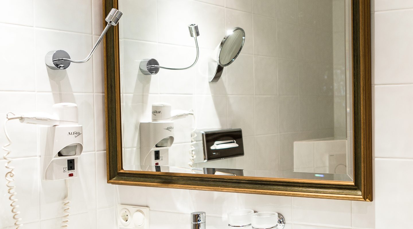 A modern bathroom vanity with a large gold-framed mirror, white sink, faucet, and a wall-mounted hairdryer.