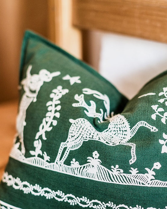 Close-up of a green throw pillow with white embroidered stag and foliage patterns.