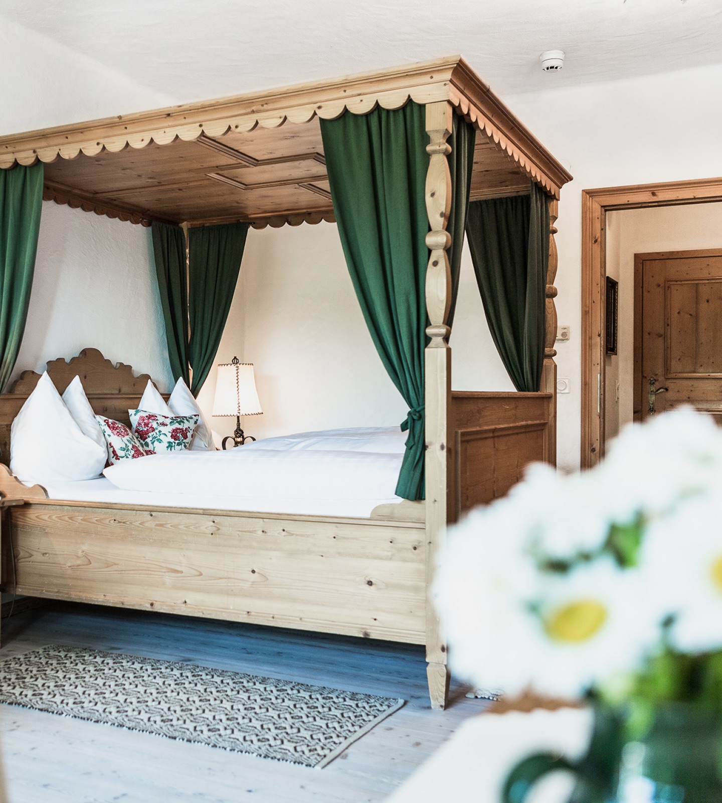 Rustic wooden four-poster bed with green curtains and white bedding in a cozy bedroom setting.