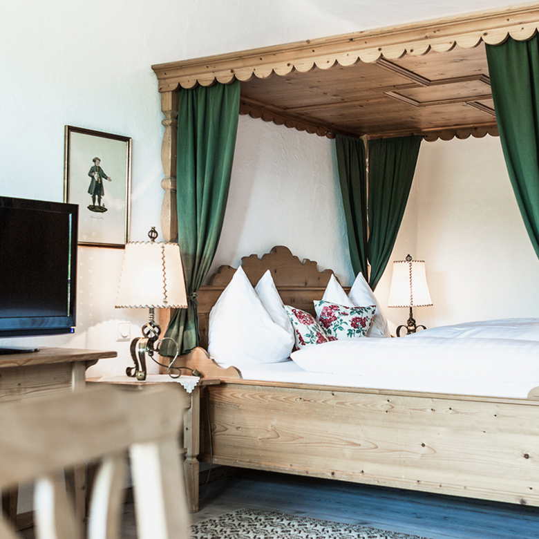 Rustic wooden four-poster bed with green curtains, white bedding, and floral pillows in a cozy bedroom.