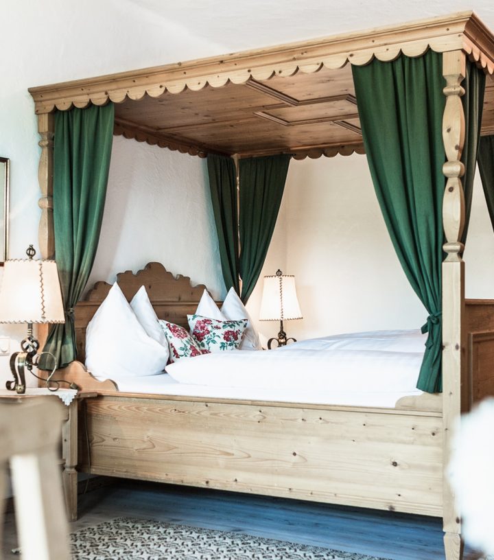 Traditional wooden four-poster bed with green curtains and white bedding in a rustic hotel room.