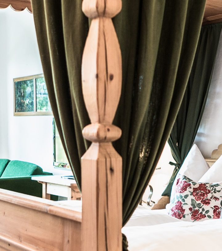 Rustic wooden four-poster bed with olive green curtains and floral pillows in a cozy bedroom.