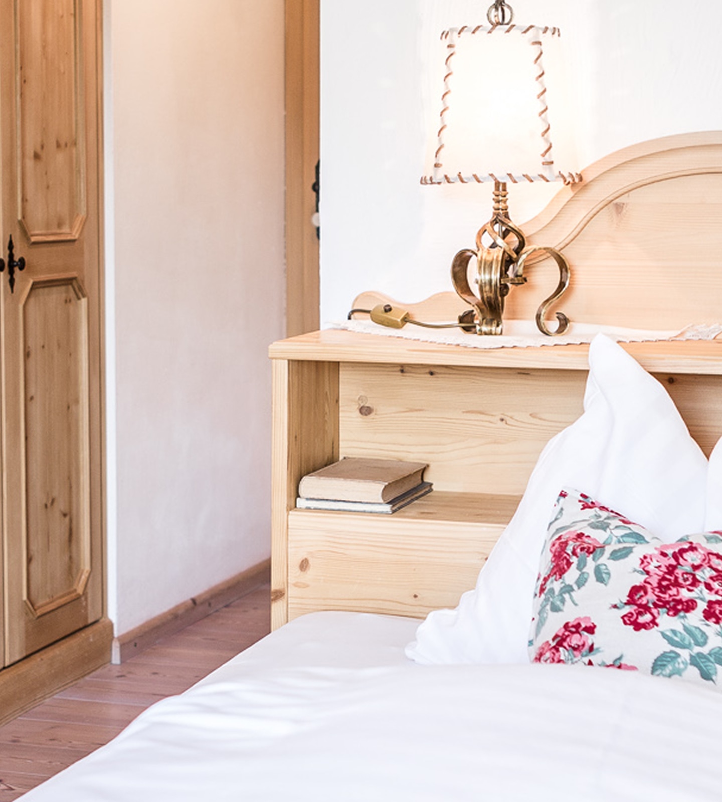 Cozy bedroom corner with a light wood headboard, a classical lamp, pillows, and a small stack of books.