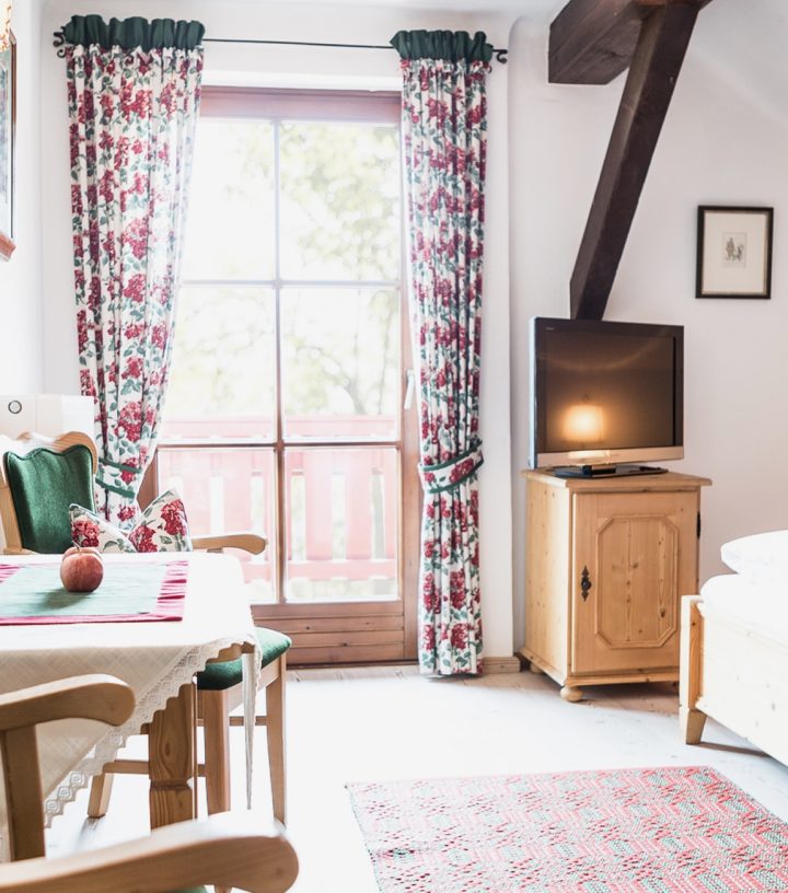 Rustic hotel bedroom with wood-frame bed, dining set, and French doors leading to a balcony.