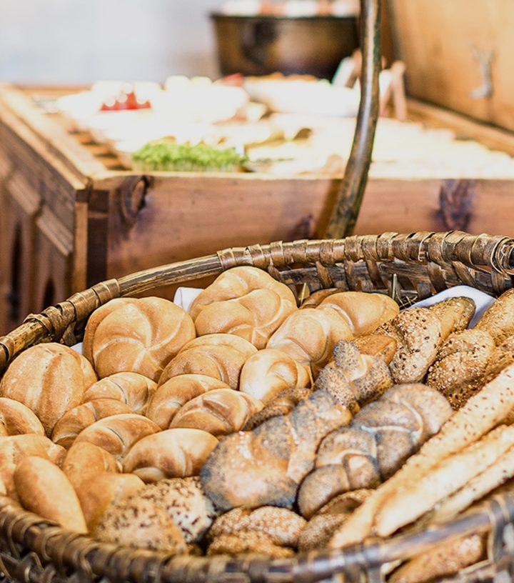 Wicker basket filled with a variety of fresh bread rolls, seeded buns, and breadsticks.
