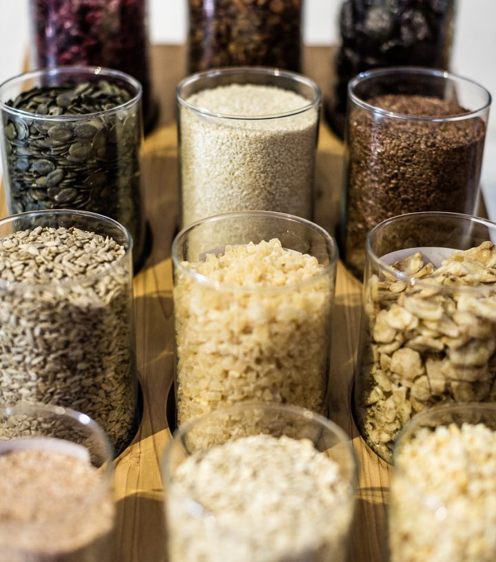 Various seeds, grains, and dried ingredients in glass jars arranged on a wooden tray.