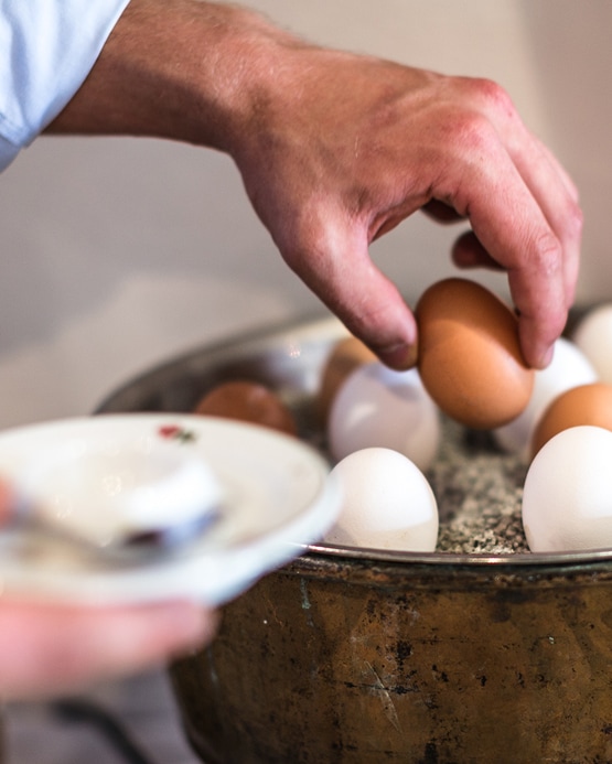 Close-up of a person's hand picking a brown egg from a bowl of white and brown eggs.