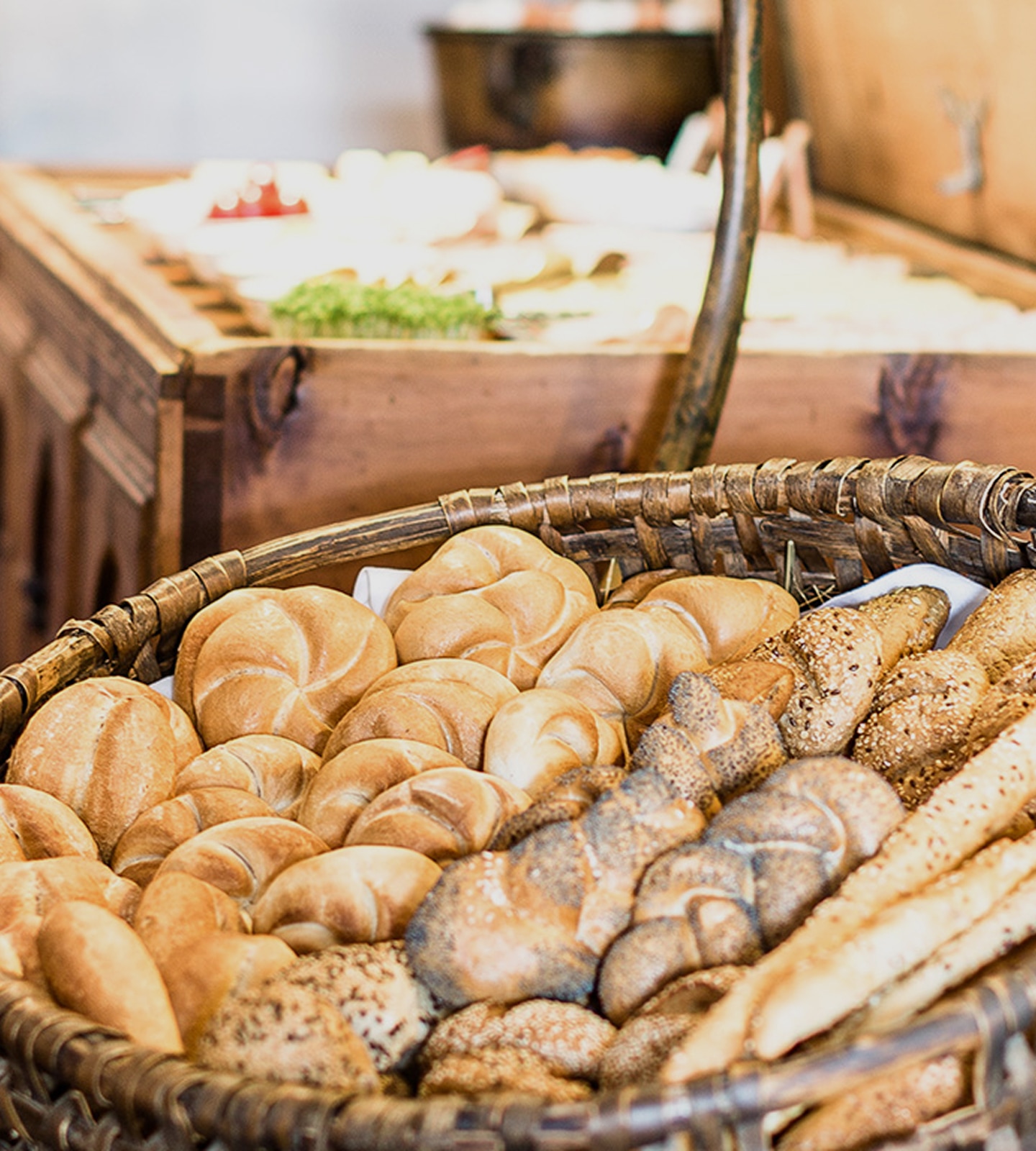 A woven basket filled with an assortment of fresh bread rolls, seeded buns, and breadsticks.