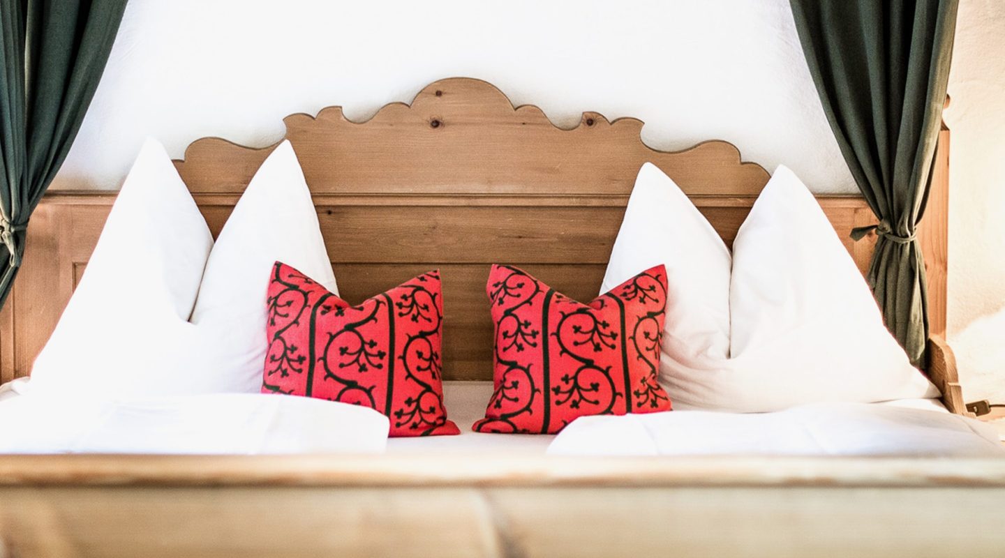 A wooden headboard with white pillows and two small, patterned red pillows on a bed.