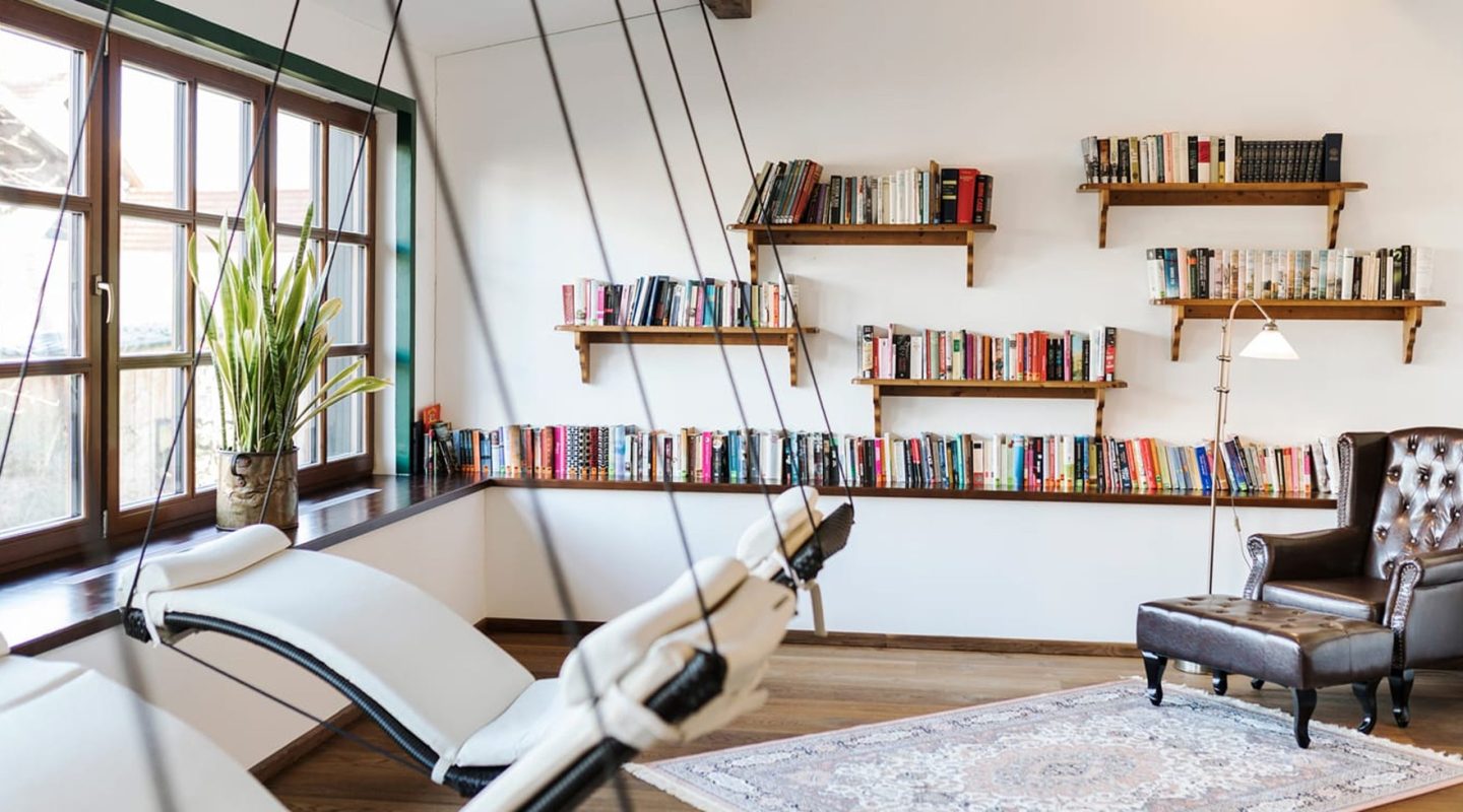 Cozy reading room with hanging white lounge chairs, bookshelves filled with books, and a brown leather armchair.