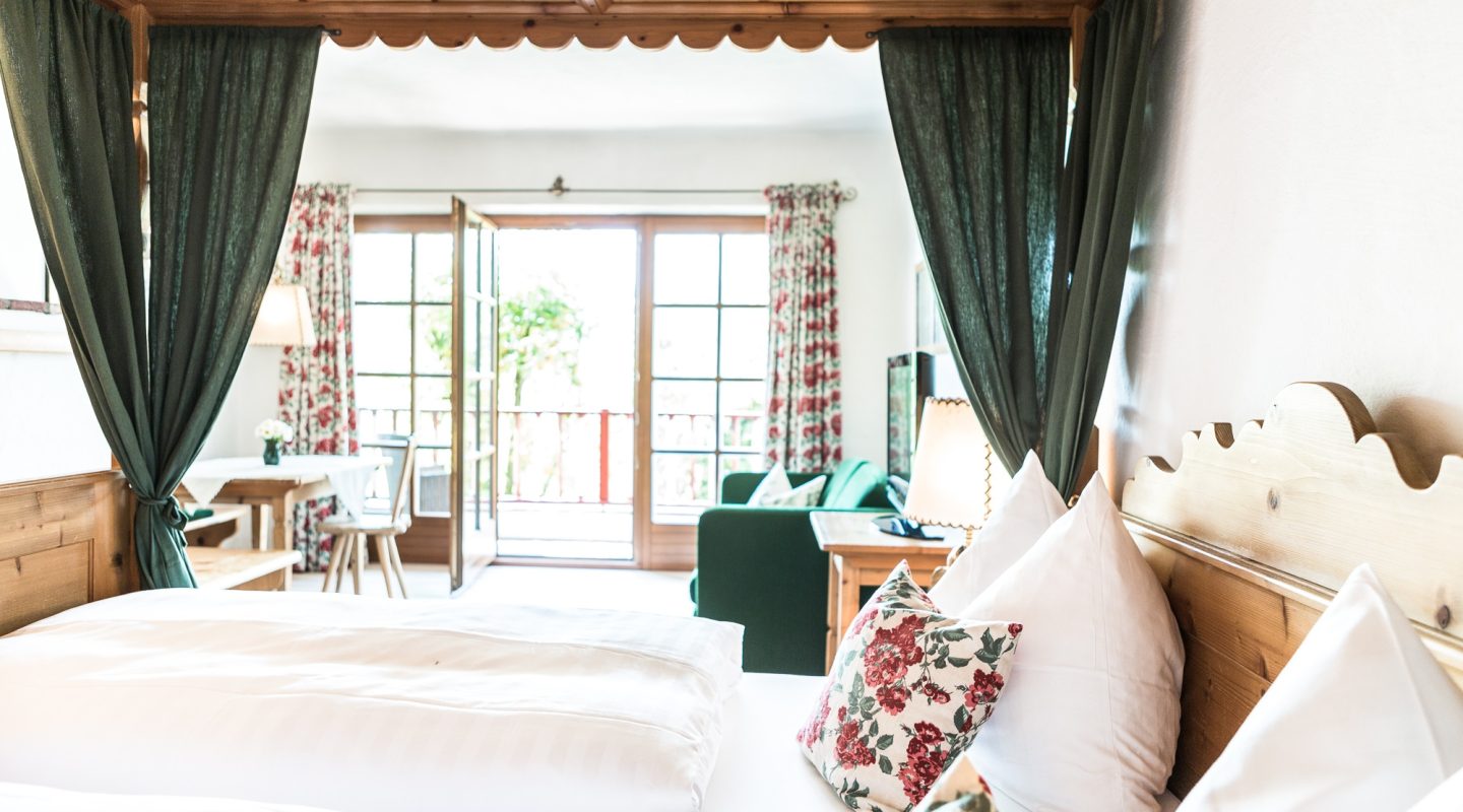 Cozy bedroom in a rustic style with a wooden four-poster bed, green curtains, and balcony doors in the background.