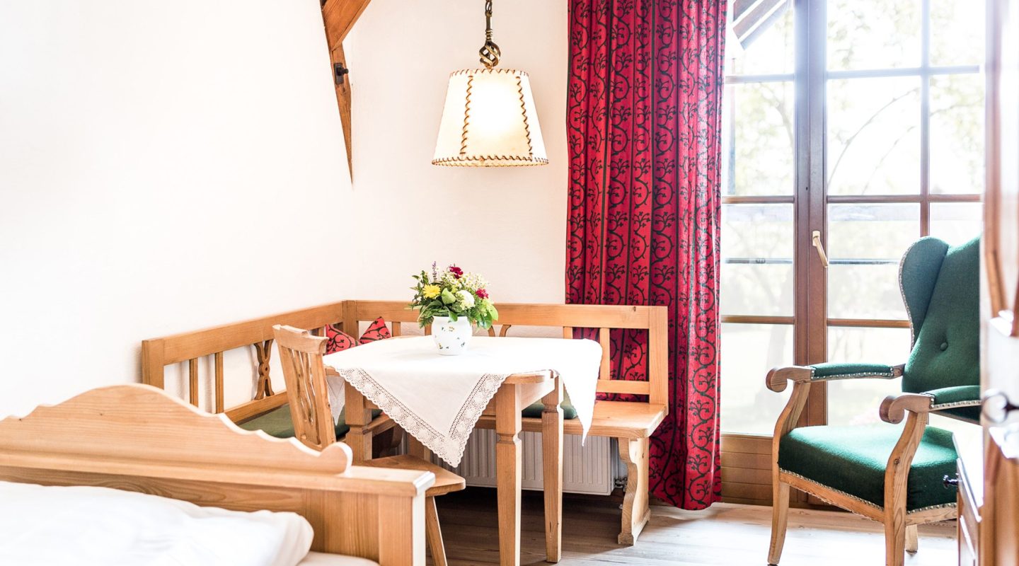 Cozy wooden dining nook with a white tablecloth, a green armchair, and a red curtain by a window.