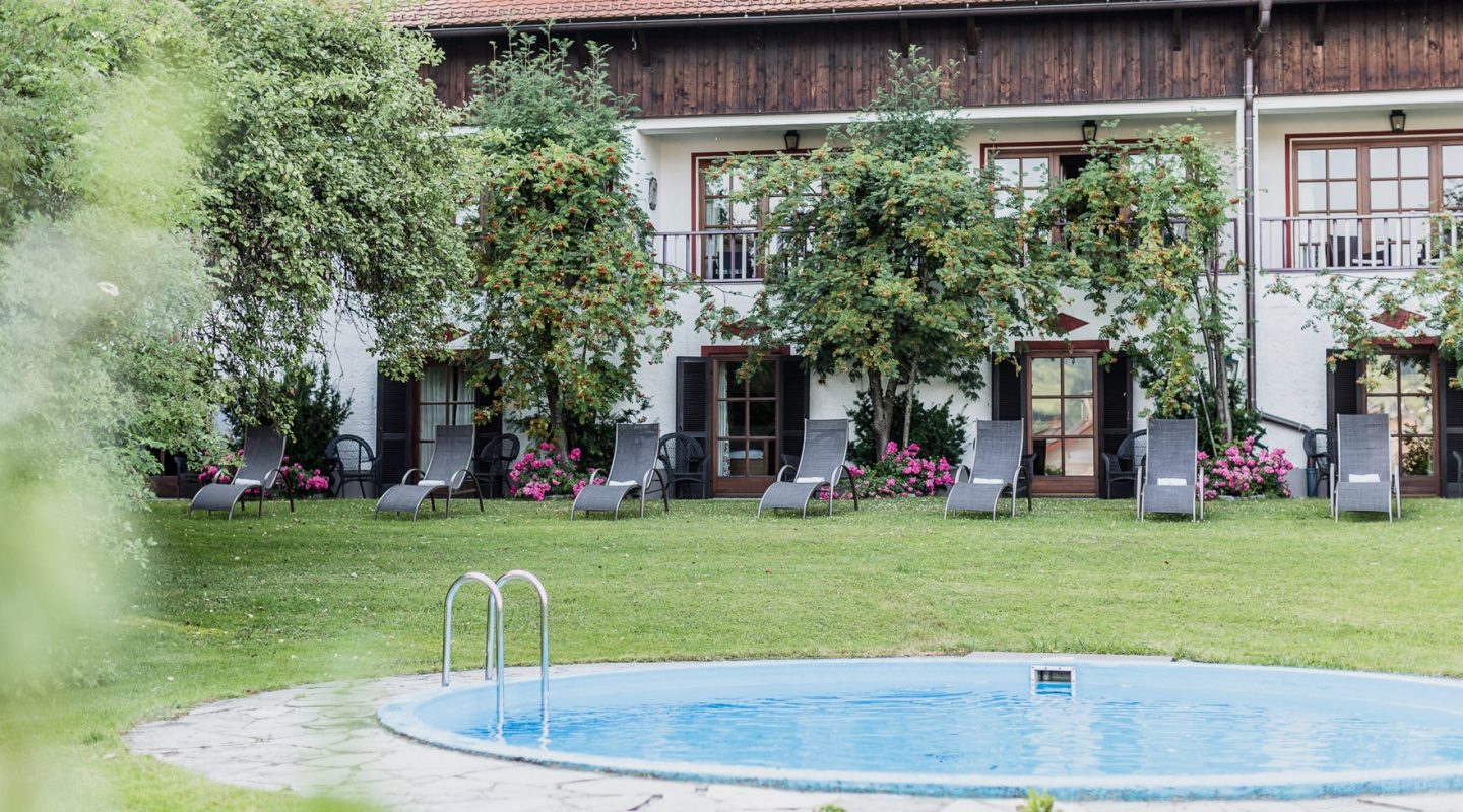 A round outdoor swimming pool on a green lawn with lounge chairs lined up in front of a white and wooden building.