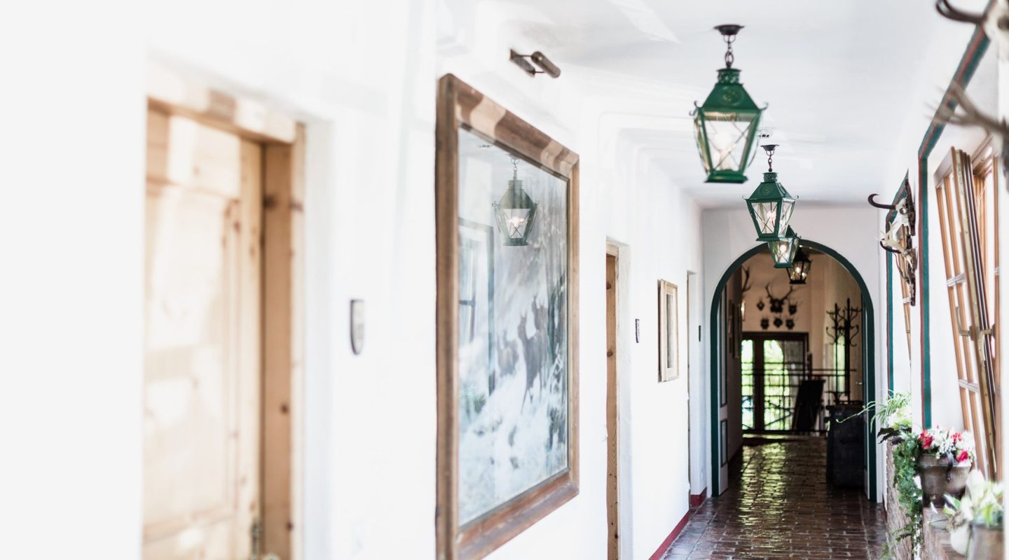 Brightly lit hallway with white walls, rustic wooden frames, and green lantern lights hanging from the ceiling.