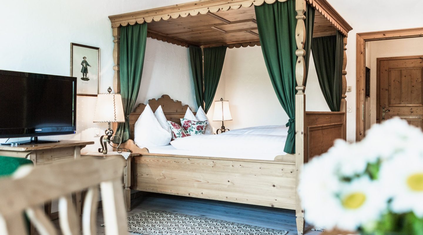 Rustic wooden four-poster bed with green curtains and white bedding in a cozy hotel room.