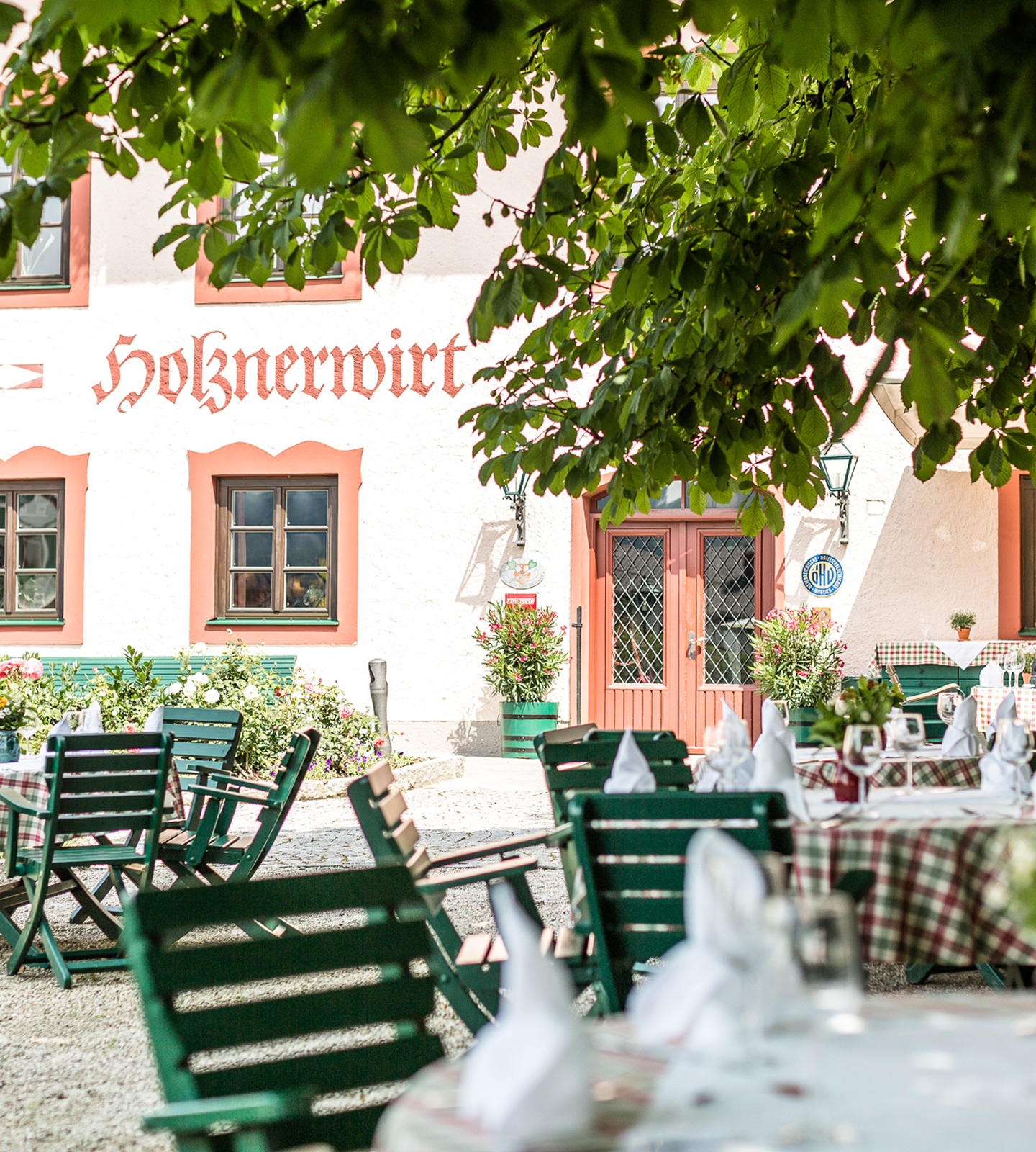 Outdoor dining area with green chairs and set tables in front of the Holznerwirt building in Salzburg.