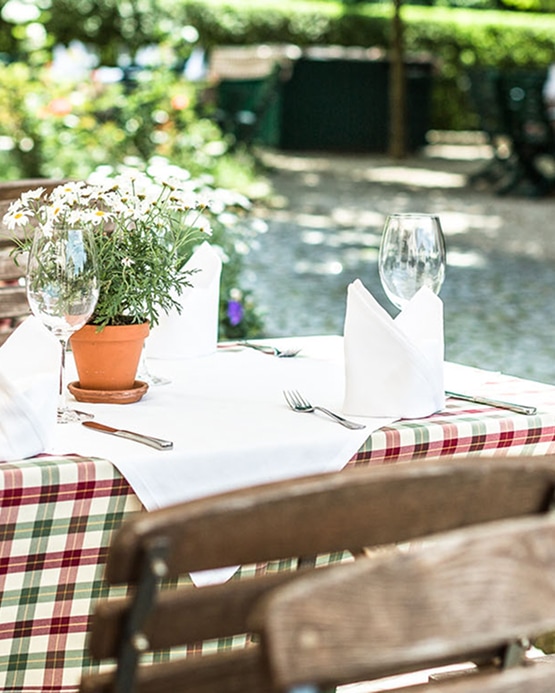 An outdoor restaurant table set with plaid tablecloth, white napkins, wine glasses, and a potted daisy centerpiece.