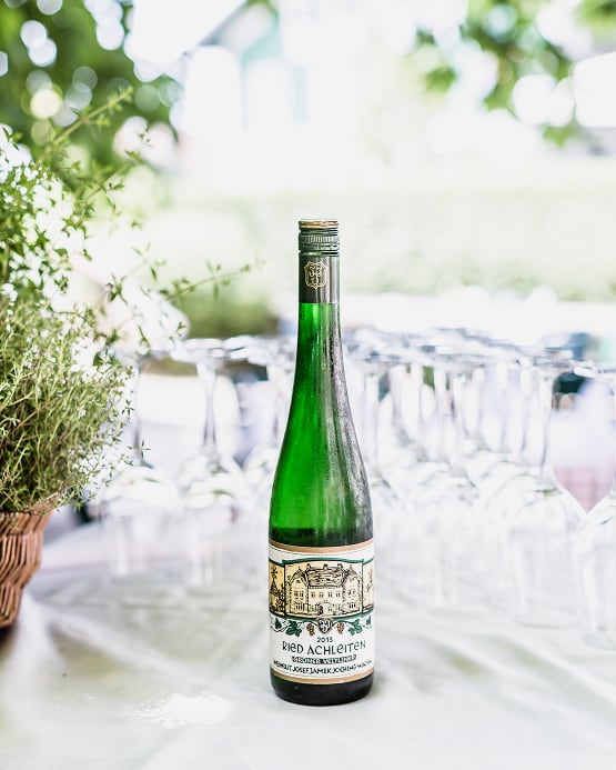 Eine grüne Flasche „Ried Achleiten“ Weißwein steht vor einer Reihe von Weingläsern im Freien.