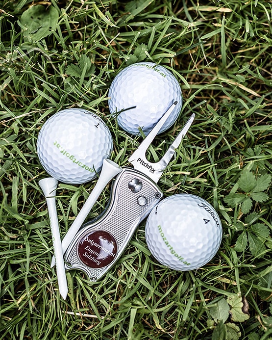 Three golf balls, two tees, and a Pitchfix divot tool on green grass.