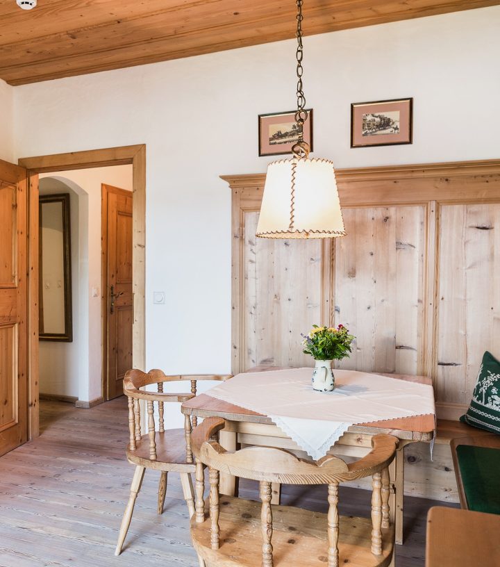 Gemütliche Essecke im Landhausstil mit Holztisch, Stühlen, Eckbank, Holzverkleidung und einer Hängelampe.