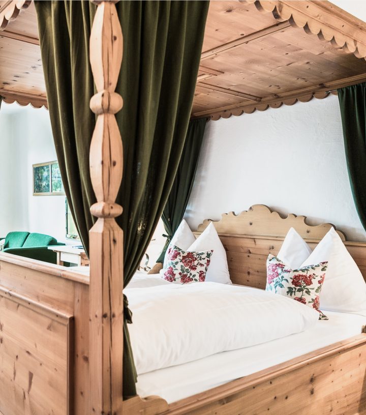 Rustikales Himmelbett aus Holz mit grünen Vorhängen und weißer Bettwäsche im alpinen Stil.