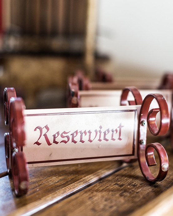 A vintage-style metal table sign on a wooden surface reading "Reserviert" in red Gothic script.