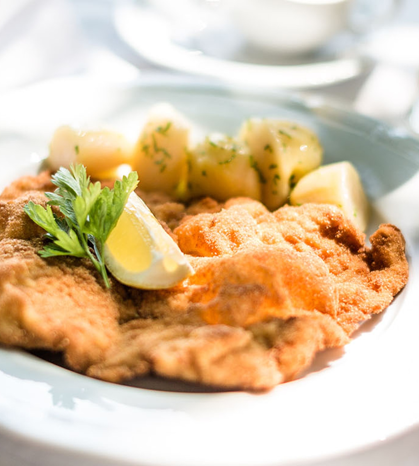 Golden-brown Wiener Schnitzel served on a white plate with parsley potatoes, a lemon wedge, and a parsley sprig.