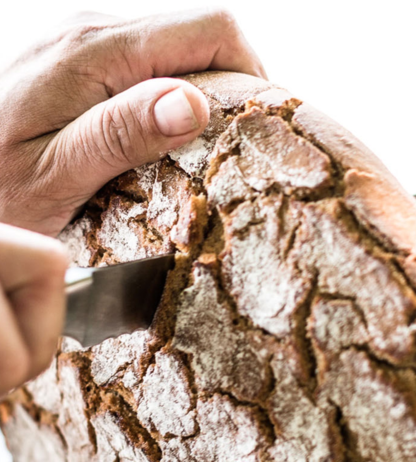 Close-up of hands cutting a loaf of crusty, artisanal sourdough bread with a serrated knife.