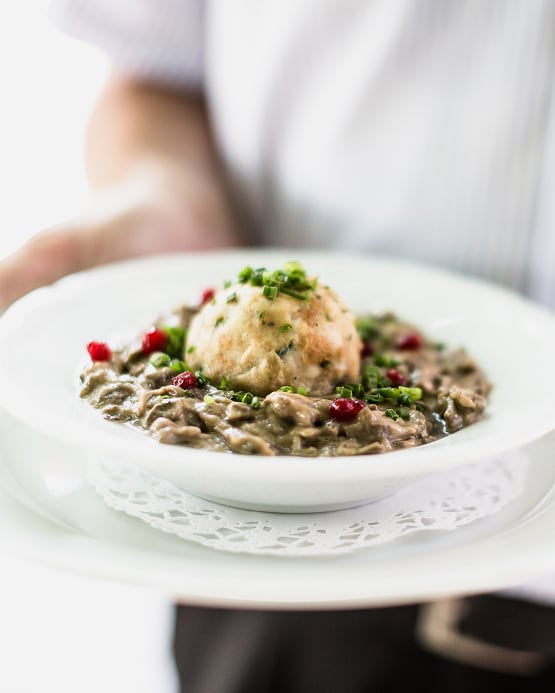 Semmelknödel in Pilzrahmsoße mit Preiselbeeren und Schnittlauch auf einem Teller serviert.
