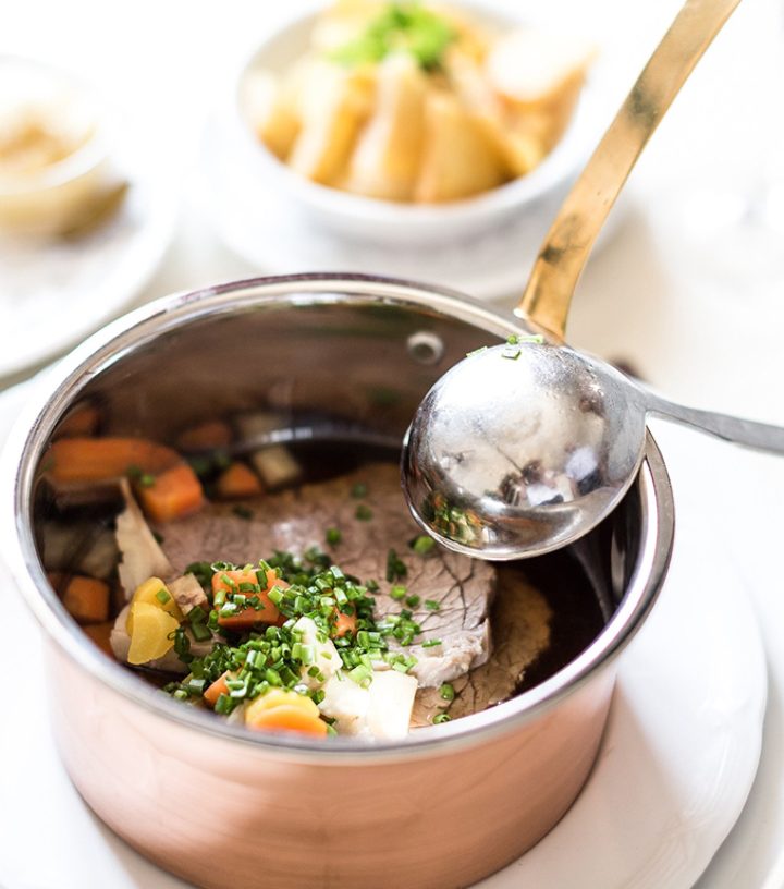 Tafelspitz, Austrian boiled beef, in a copper pot with broth, vegetables, and chives, served with a ladle.
