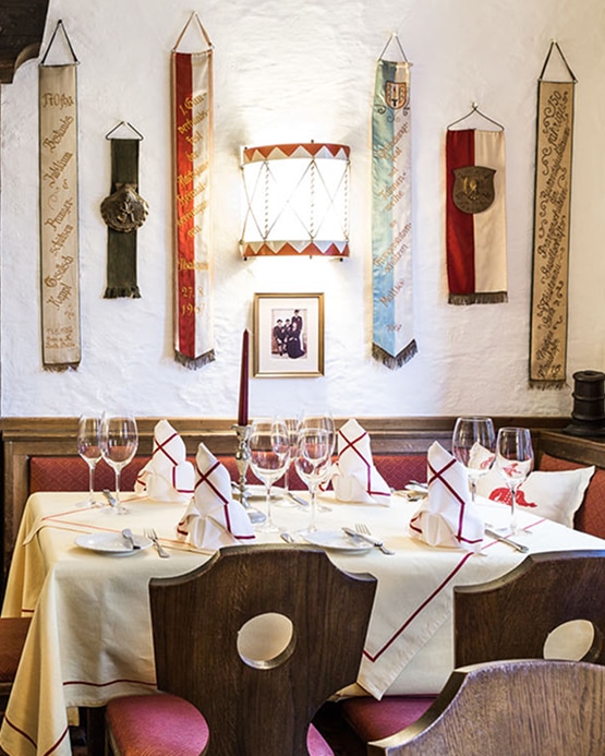 A set dining table with red-bordered napkins and wine glasses under a wall decorated with historic banners.