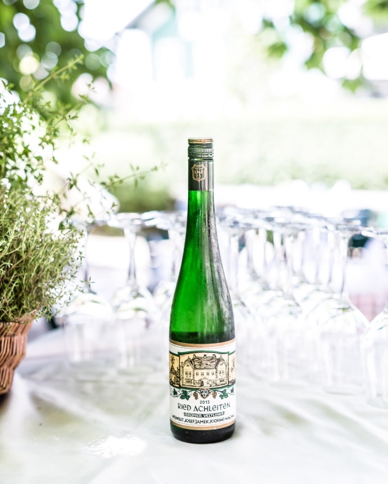 A bottle of Ried Achleiten Grüner Veltliner wine on a table surrounded by empty wine glasses.