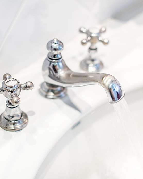 Water running from a classic chrome faucet into a white porcelain sink with vintage cross handles.
