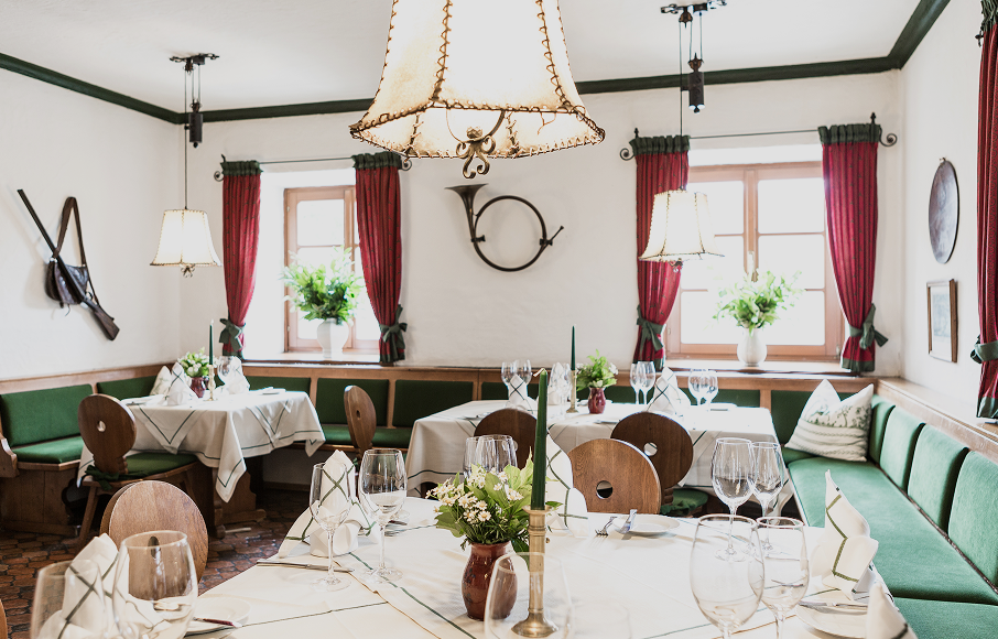 Charming rustic dining room with white tablecloths, green cushioned benches, and red curtains.