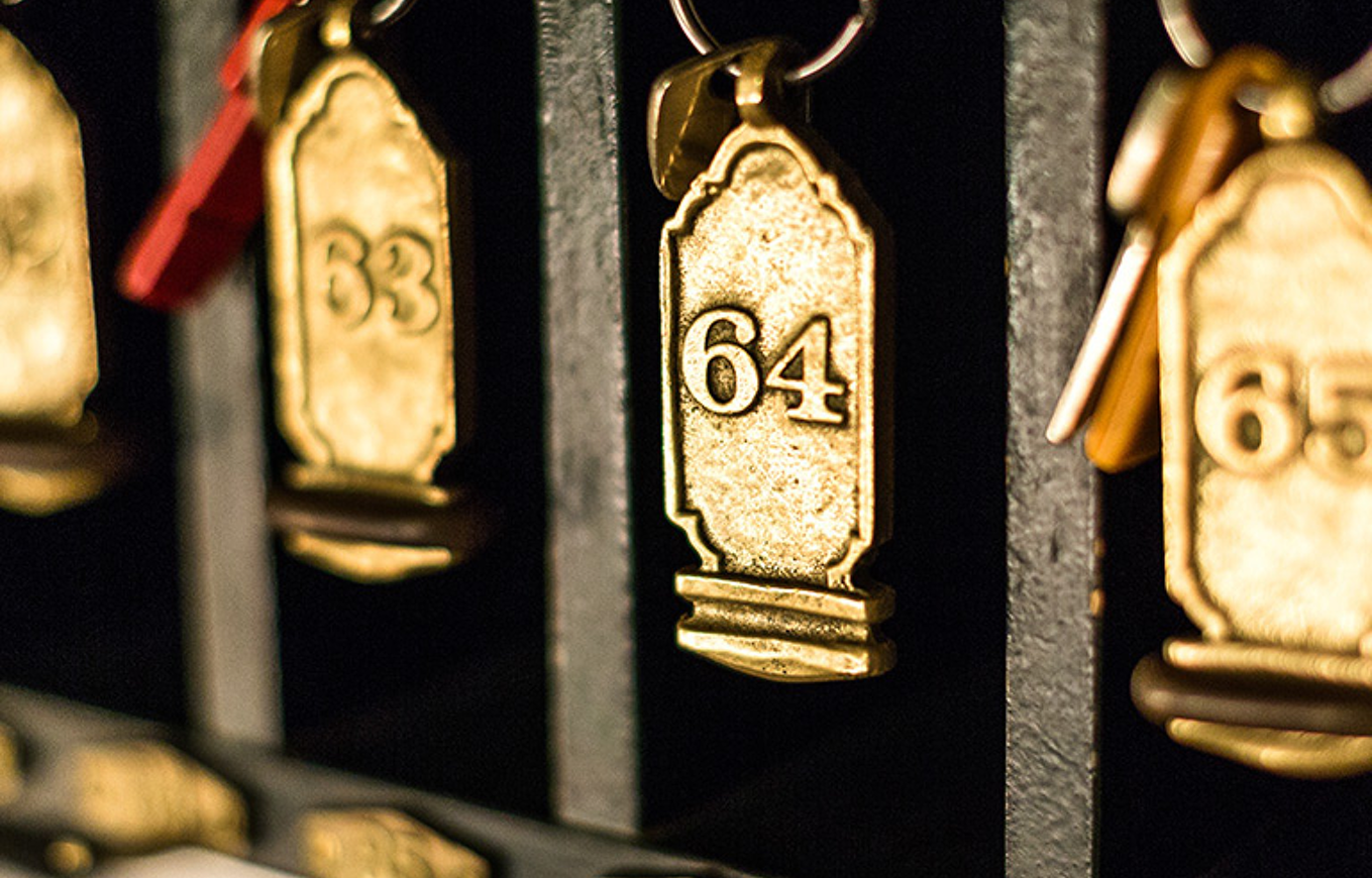 Close-up of vintage brass hotel key fobs hanging in numerical order, featuring number 64.