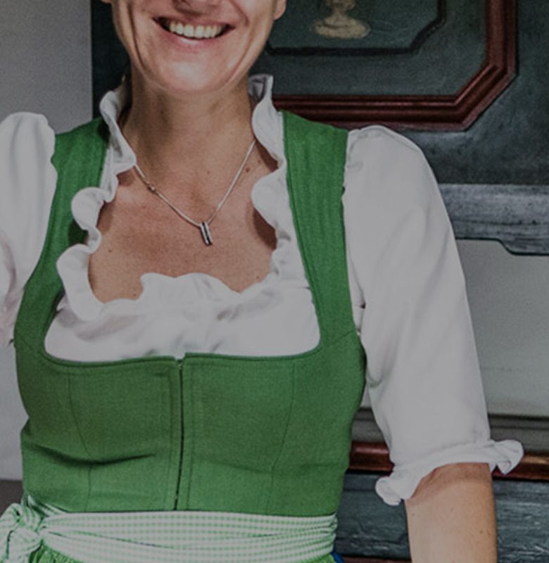 A smiling woman wearing a traditional green dirndl and white blouse.