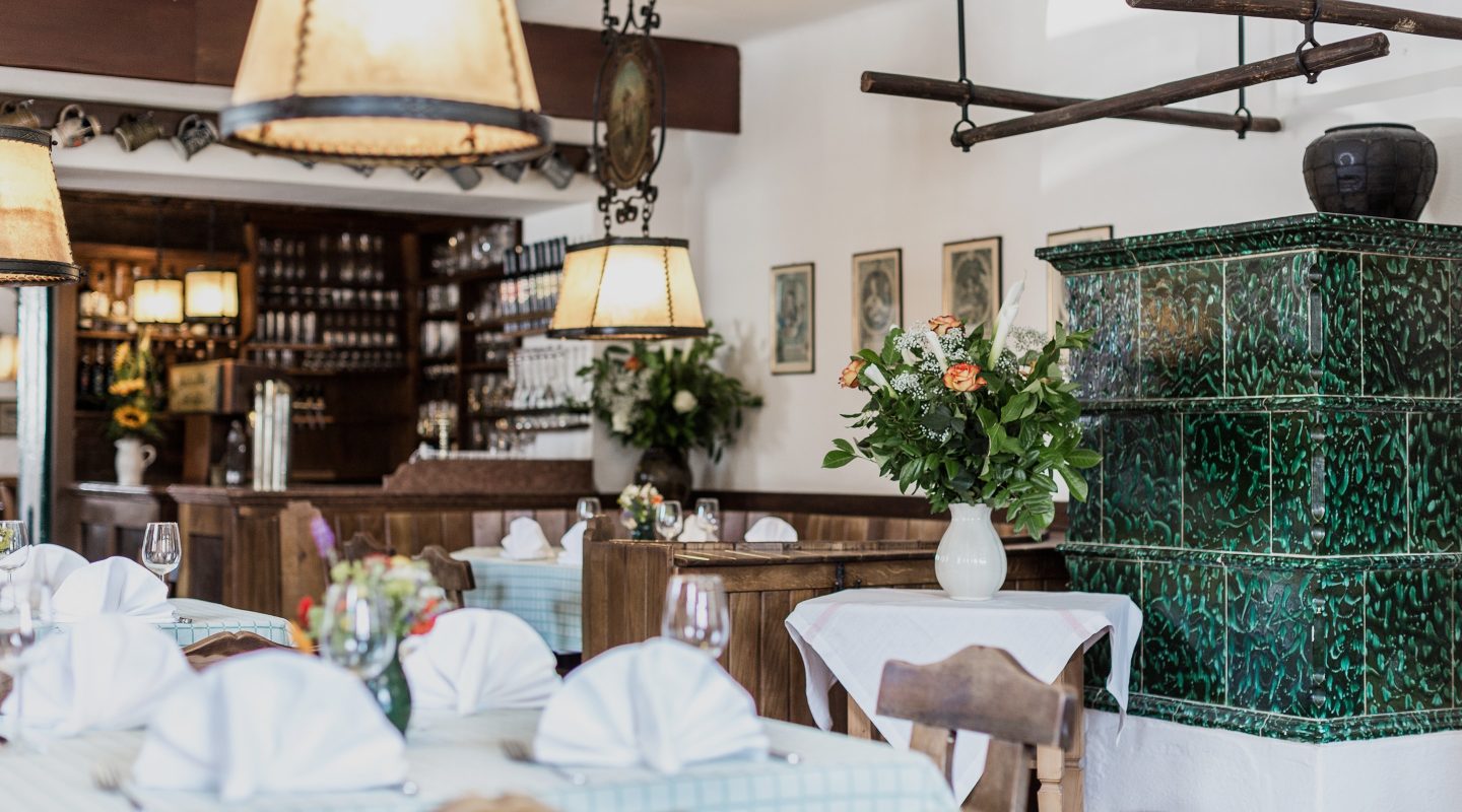 Cozy, traditional German restaurant interior with set tables, wooden chairs, and a green tiled stove.