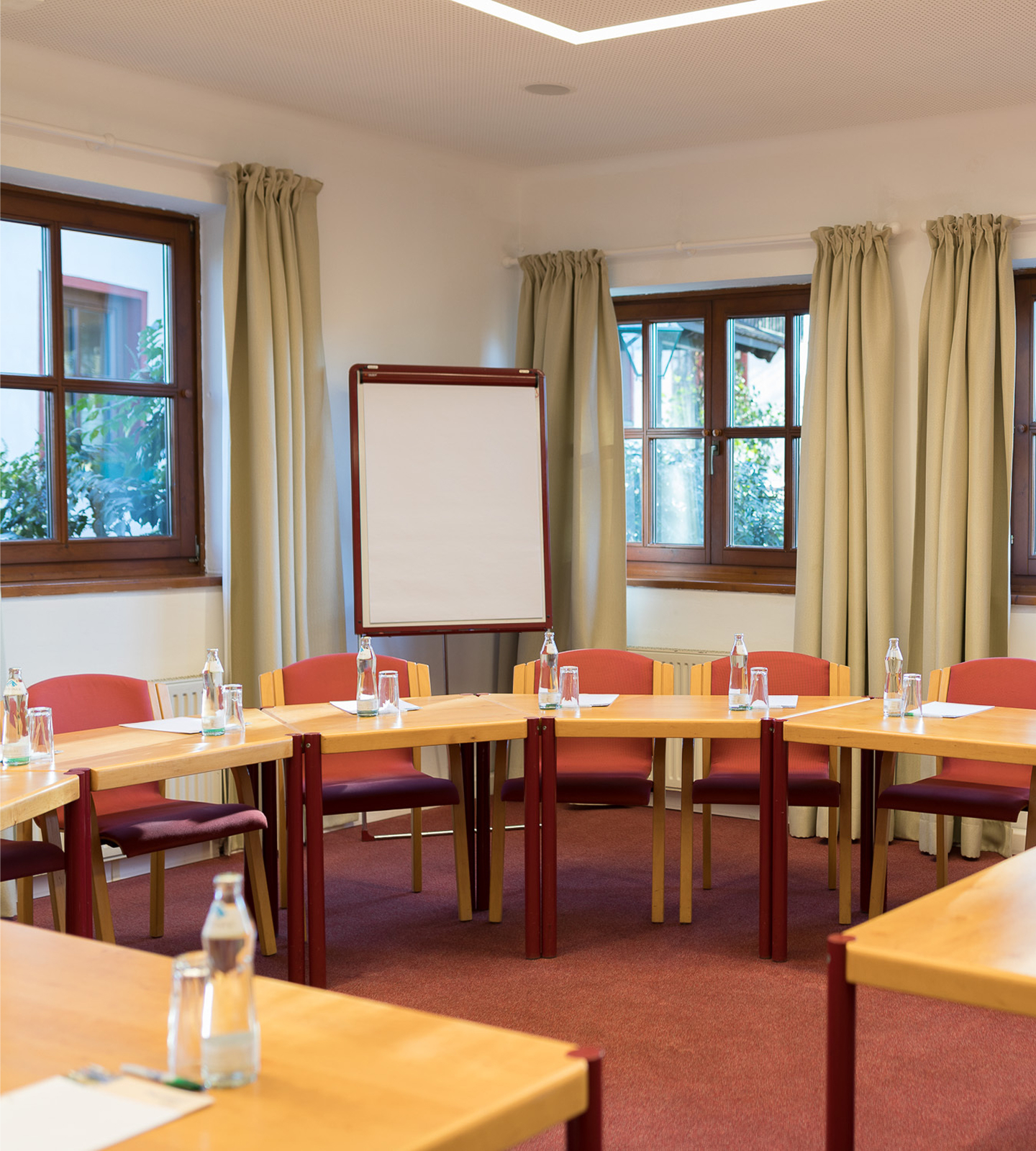 A seminar room set up with a semi-circle of wooden tables, red chairs, water bottles, and a whiteboard.