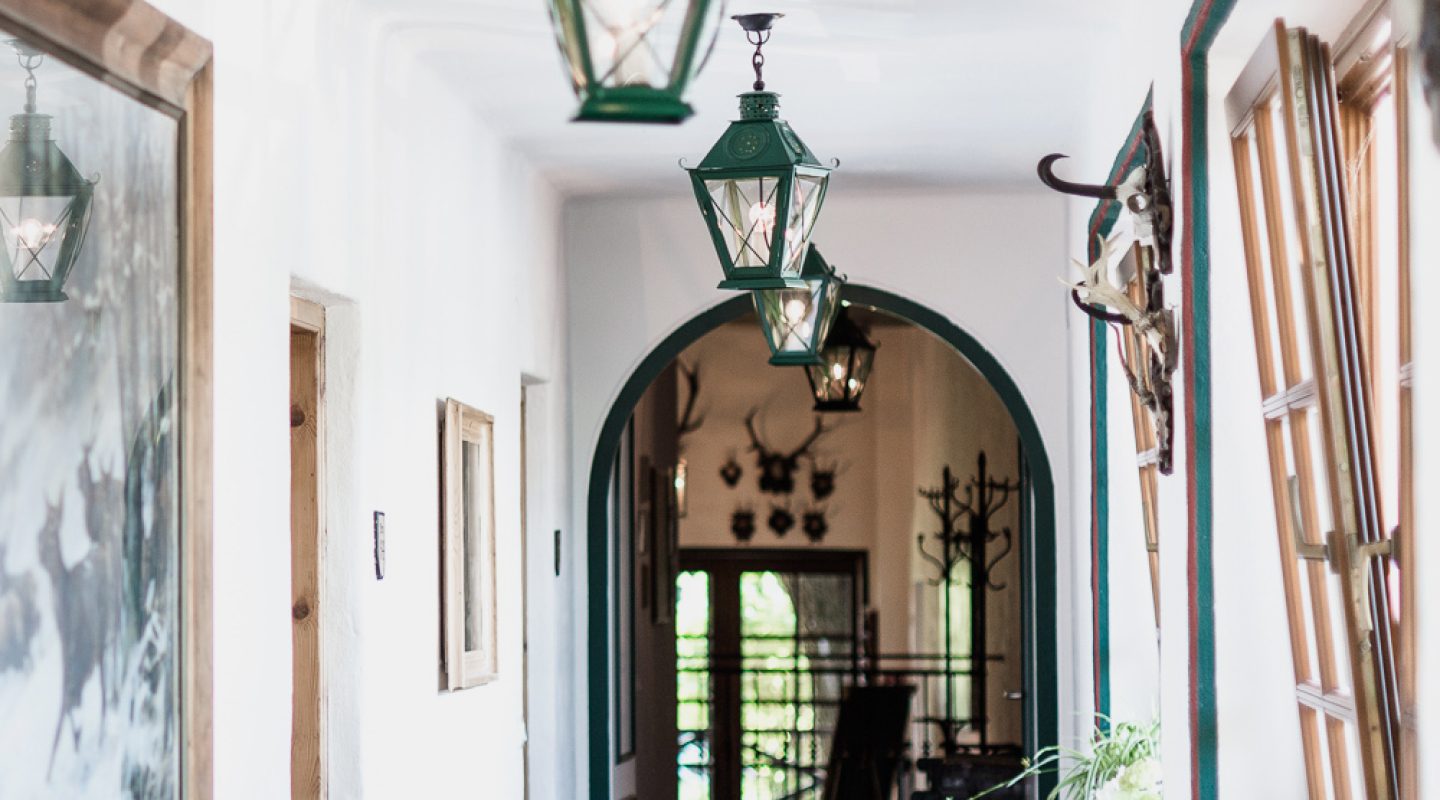 A long white hallway with green hanging lanterns, a brick floor, and an arched doorway leading to another room.
