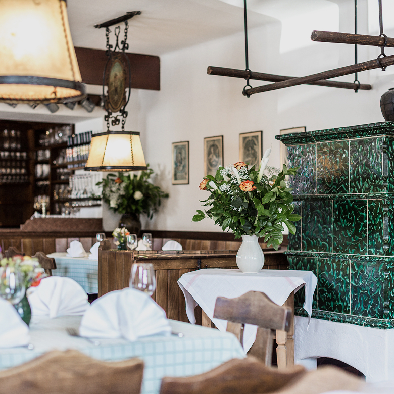 Traditional restaurant interior with set tables, a bouquet of flowers, and a classic green tiled stove.