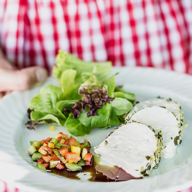 A plate of herb-crusted goat cheese slices, fresh lettuce, and diced vegetable salad with balsamic dressing.
