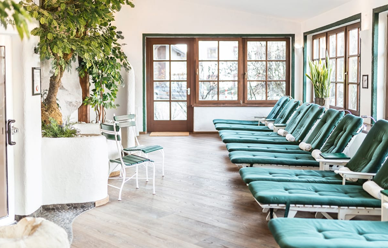 A row of green spa lounge chairs lined up in a bright room with wooden floors and large windows.
